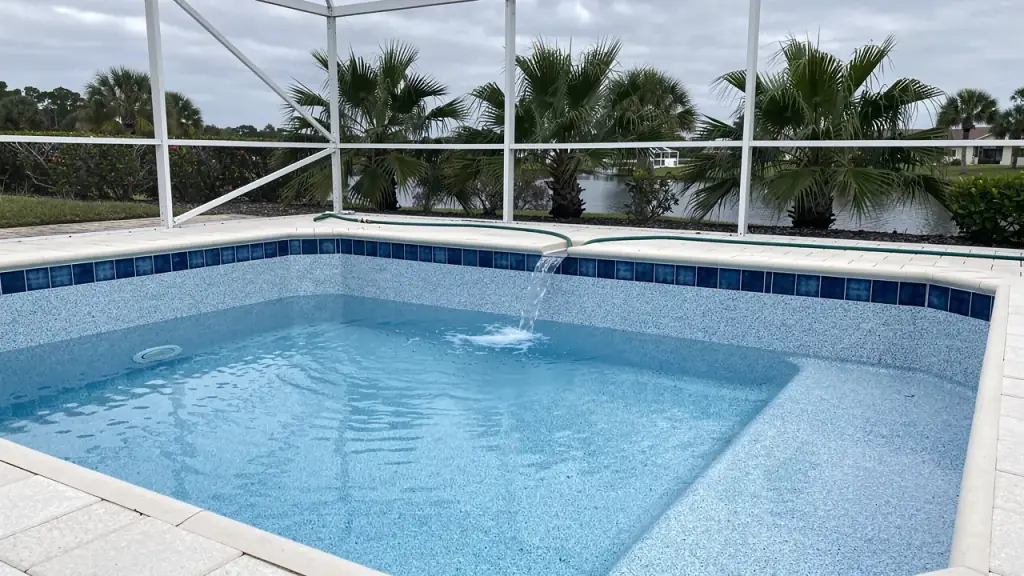 Freshly resurfaced pebble pool refilling inside a screened lanai, new blue waterline tile